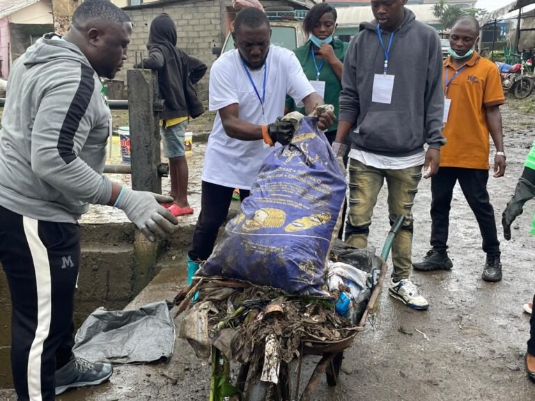 Volunteers wearing gloves lift a sack of collected waste during a cleanup.
