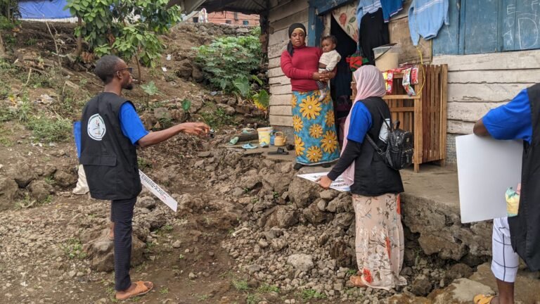 Outreach workers speak with a resident outside a home and share printed information.
