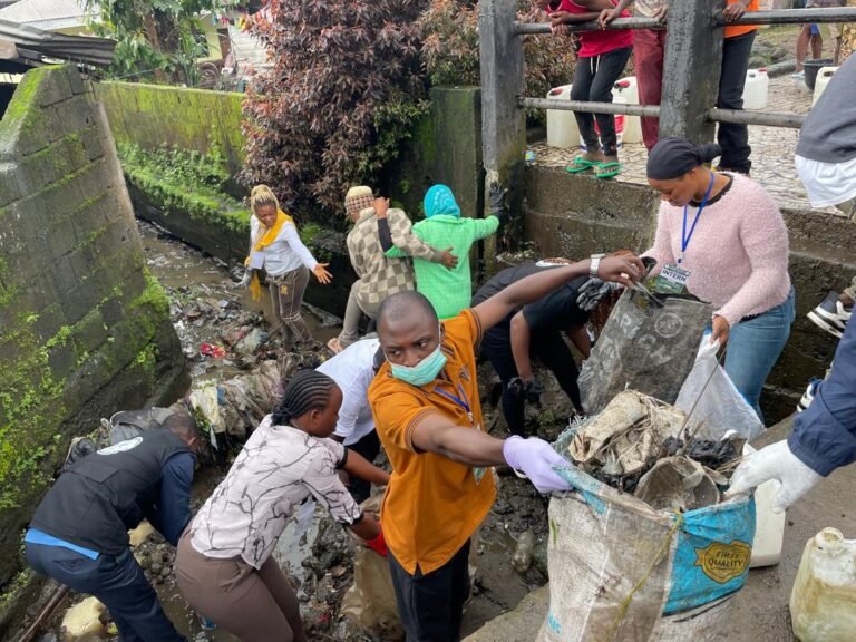Volunteers gather waste into sacks beside a drainage channel.