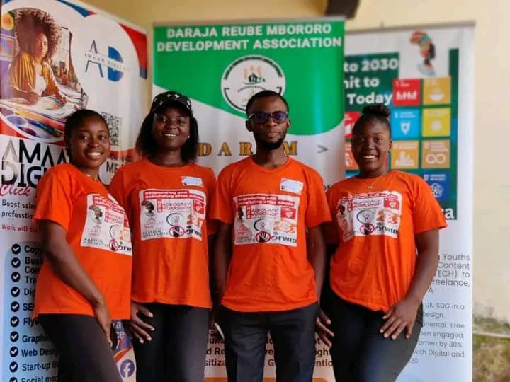 Four campaign participants in orange shirts stand in front of an organizational banner.