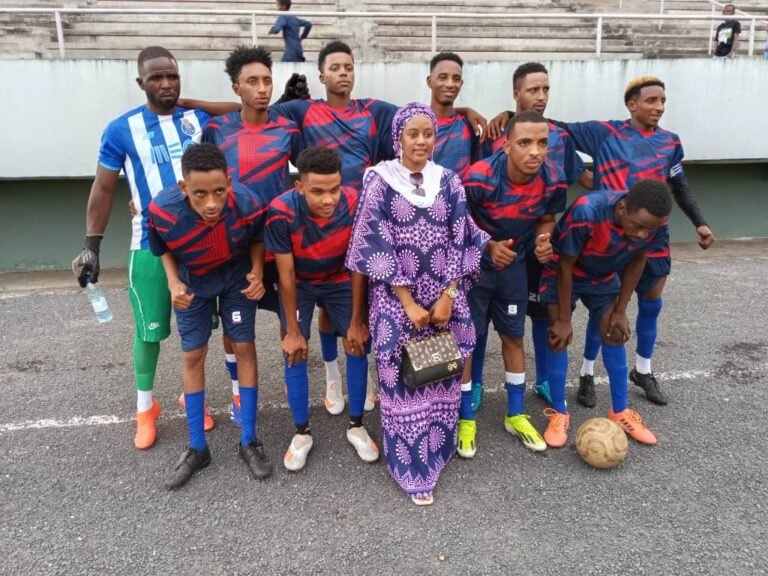 A football team and organizers pose together beside the pitch.