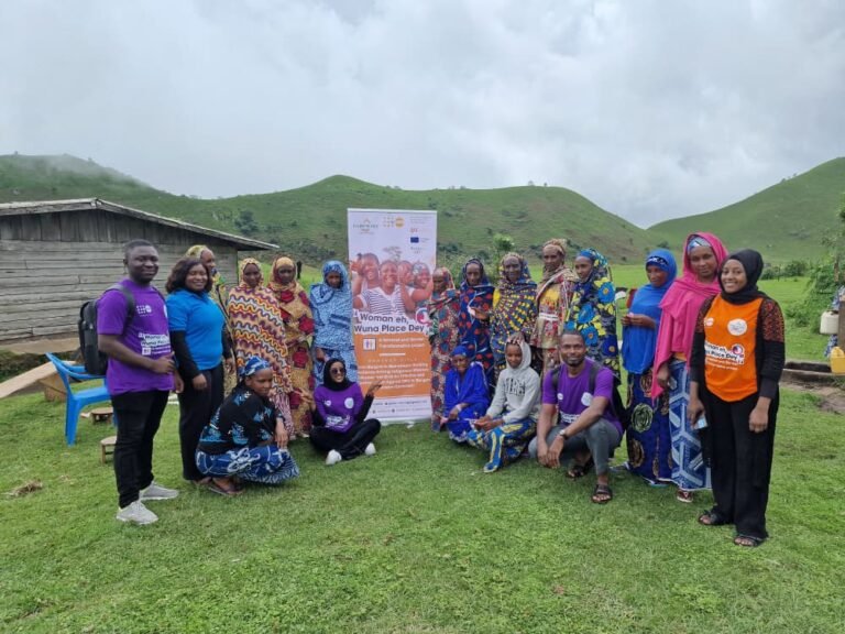 Community members and facilitators pose on a grassy hillside beside project banners.