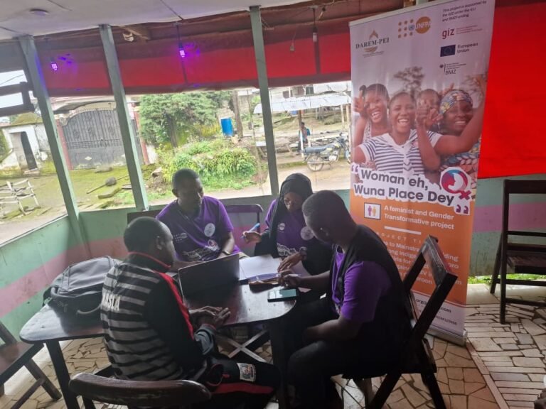 A small group meets around a table indoors beside a project banner.